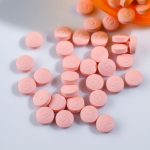 scattered pink pills on a white surface with an orange container