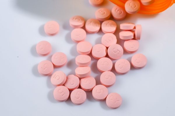scattered pink pills on a white surface with an orange container