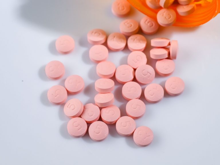 scattered pink pills on a white surface with an orange container