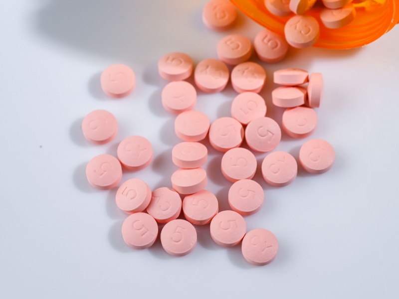 scattered pink pills on a white surface with an orange container
